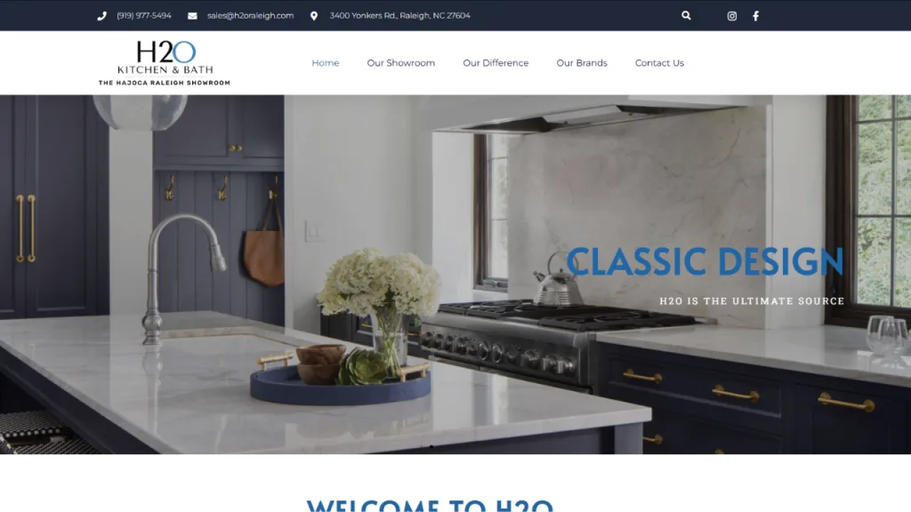 A modern kitchen with navy blue cabinetry and a large island featuring a round, white marble countertop. A vase of flowers is placed on the island, and a stainless steel range hood is visible above the stove. The design reflects a blend of classic and contemporary web design elements.